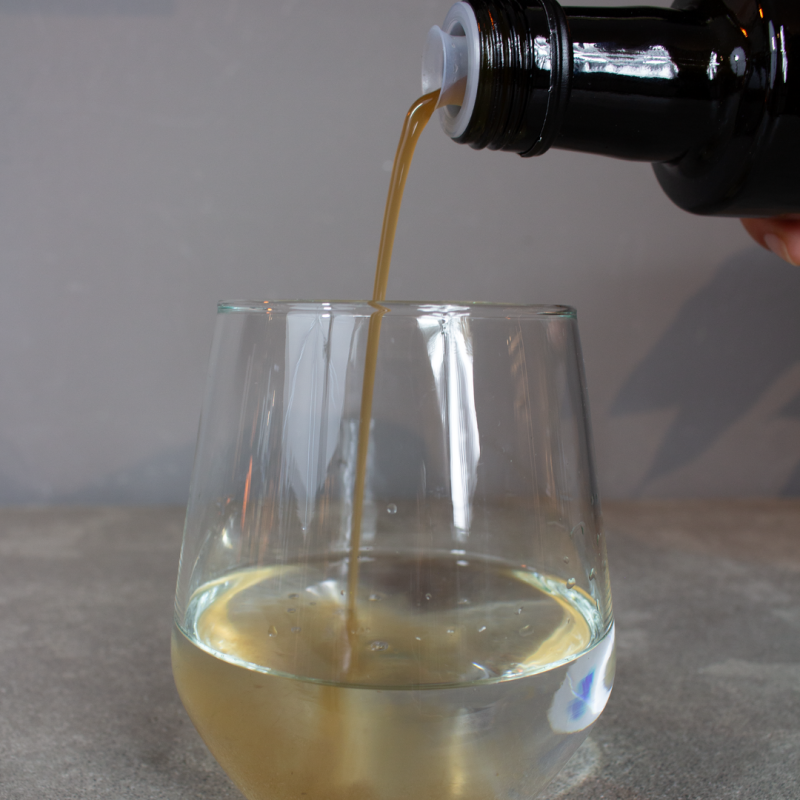 NUI NONI Essig wird aus der Flasche in ein Glas mit hellem Getränk gegossen