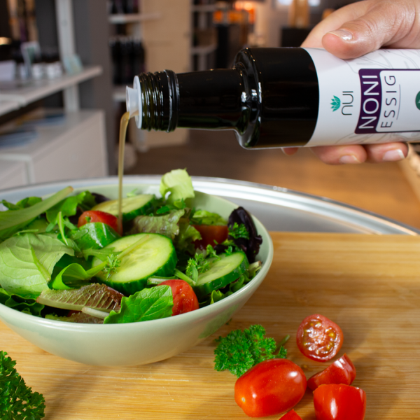 NUI NONI Essig wird aus der Flasche über eine Schüssel mit Salat und Tomaten gegossen